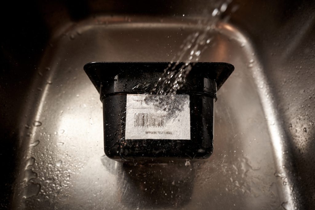 container with a bar code label in a sink with water sprayed on it 
