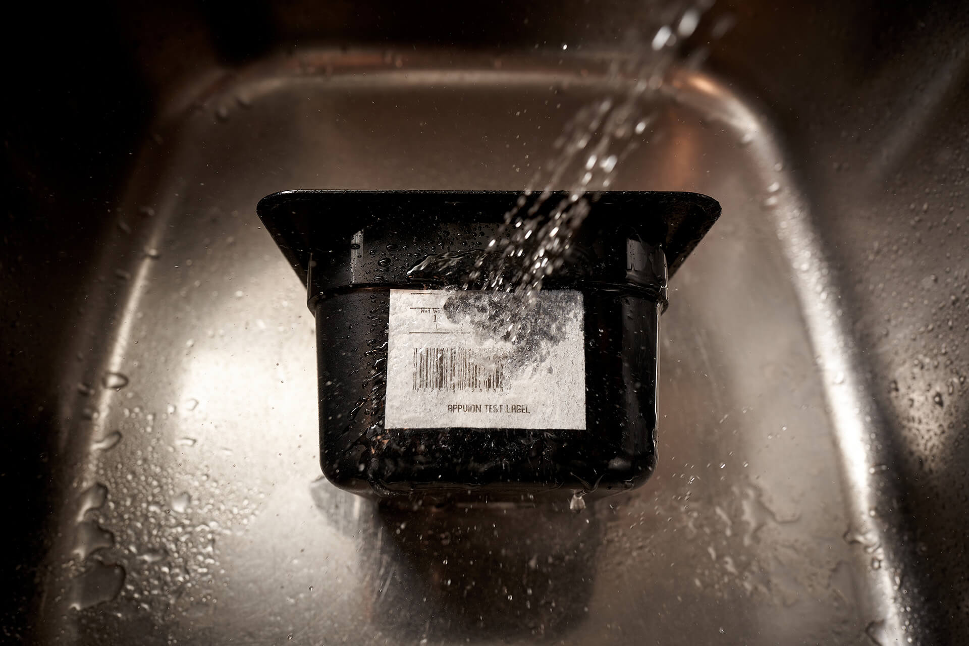 Water runs into a sink, hitting the label on a plastic bin