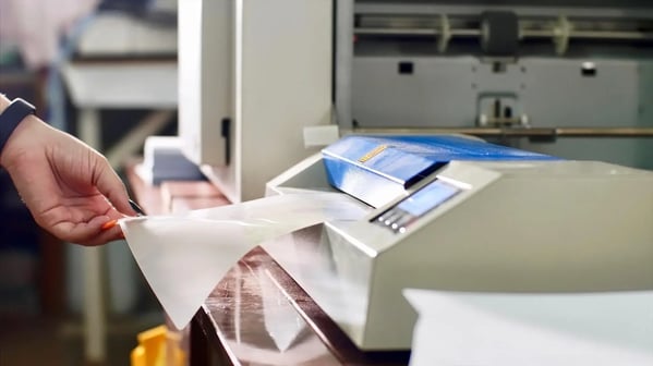 Person removing a piece of synthetic paper from a printer